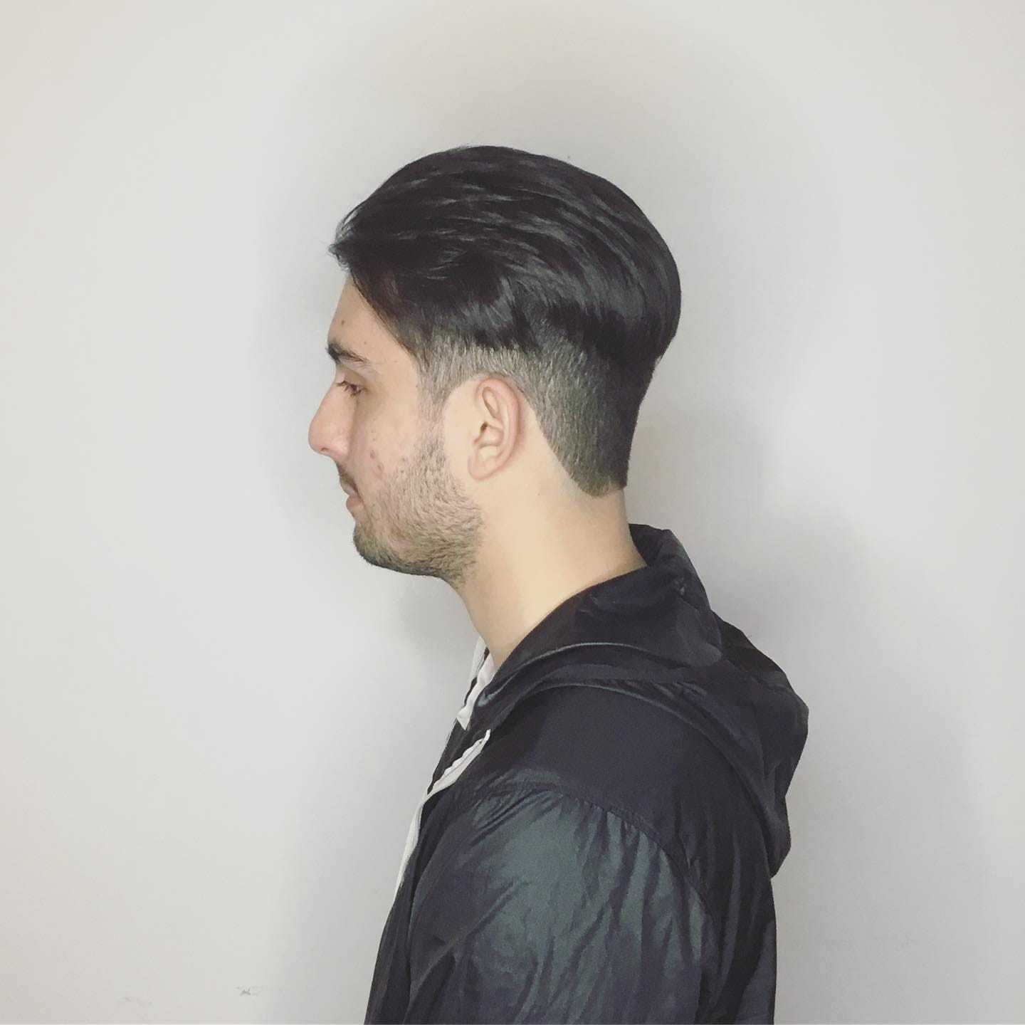 Man in profile with short, dark hair wearing a black jacket against a white background.