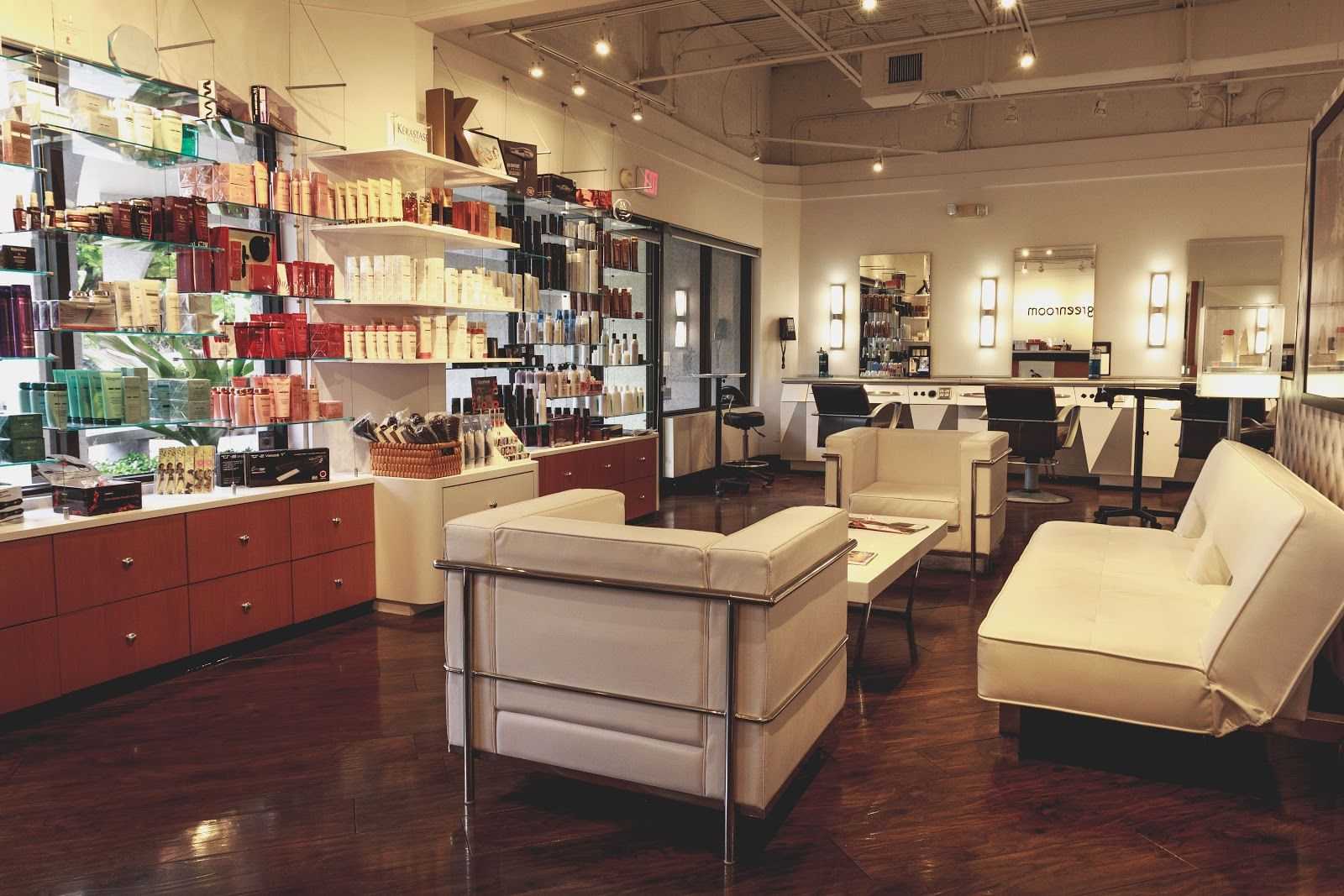 Modern salon interior with white seating, product displays, and hair styling stations.
