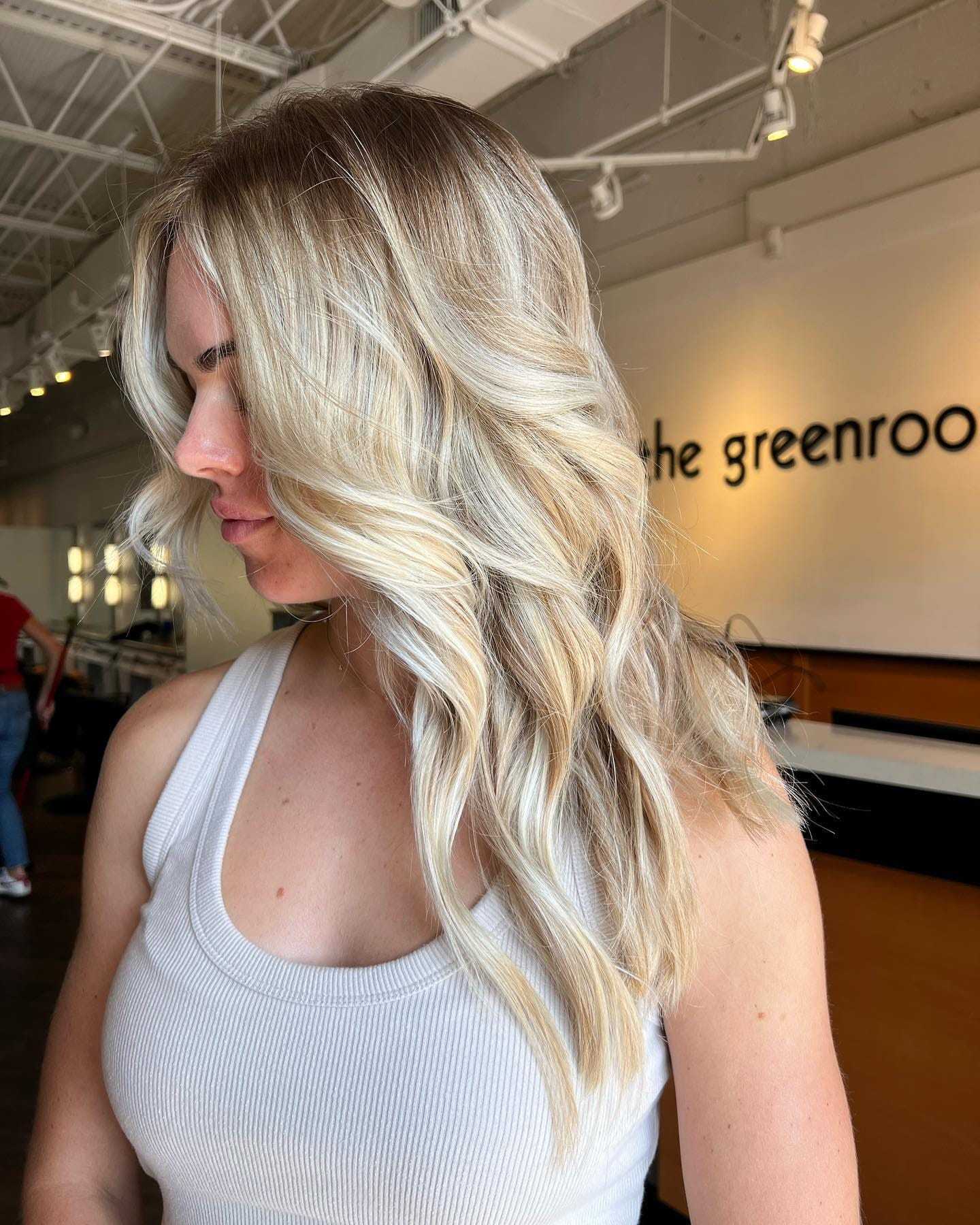 Blonde woman with wavy hair in a salon, wearing a white tank top.