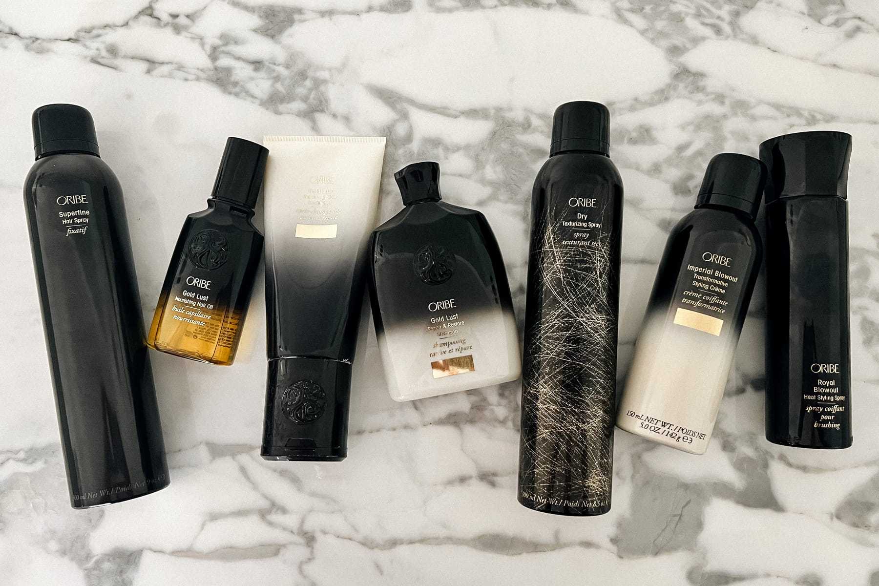 Haircare products on a marble surface, featuring various Oribe bottles and tubes.