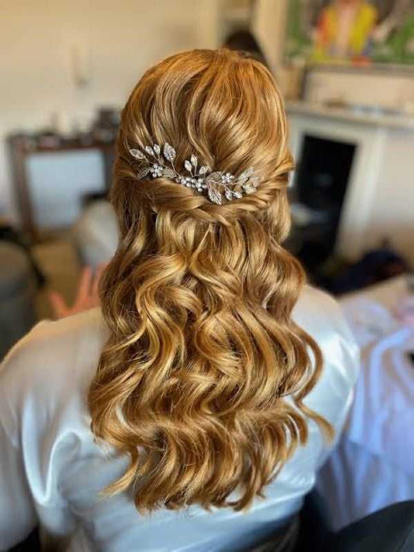 Elegant long hairstyle with curls and floral hair accessory in a cozy room background.