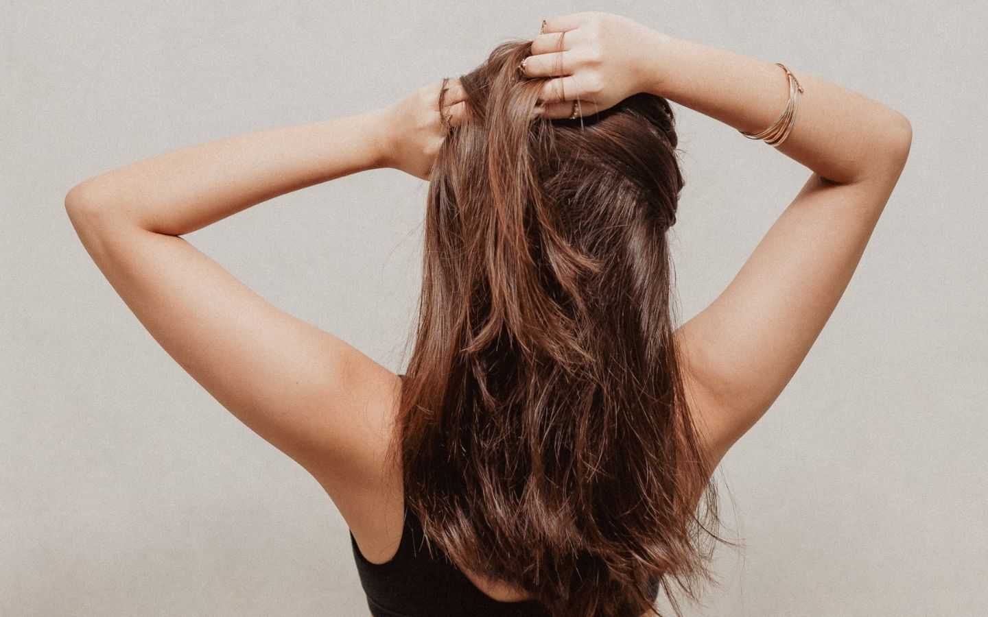 Person with long brown hair, back view, hands lifting hair, wearing bracelets.