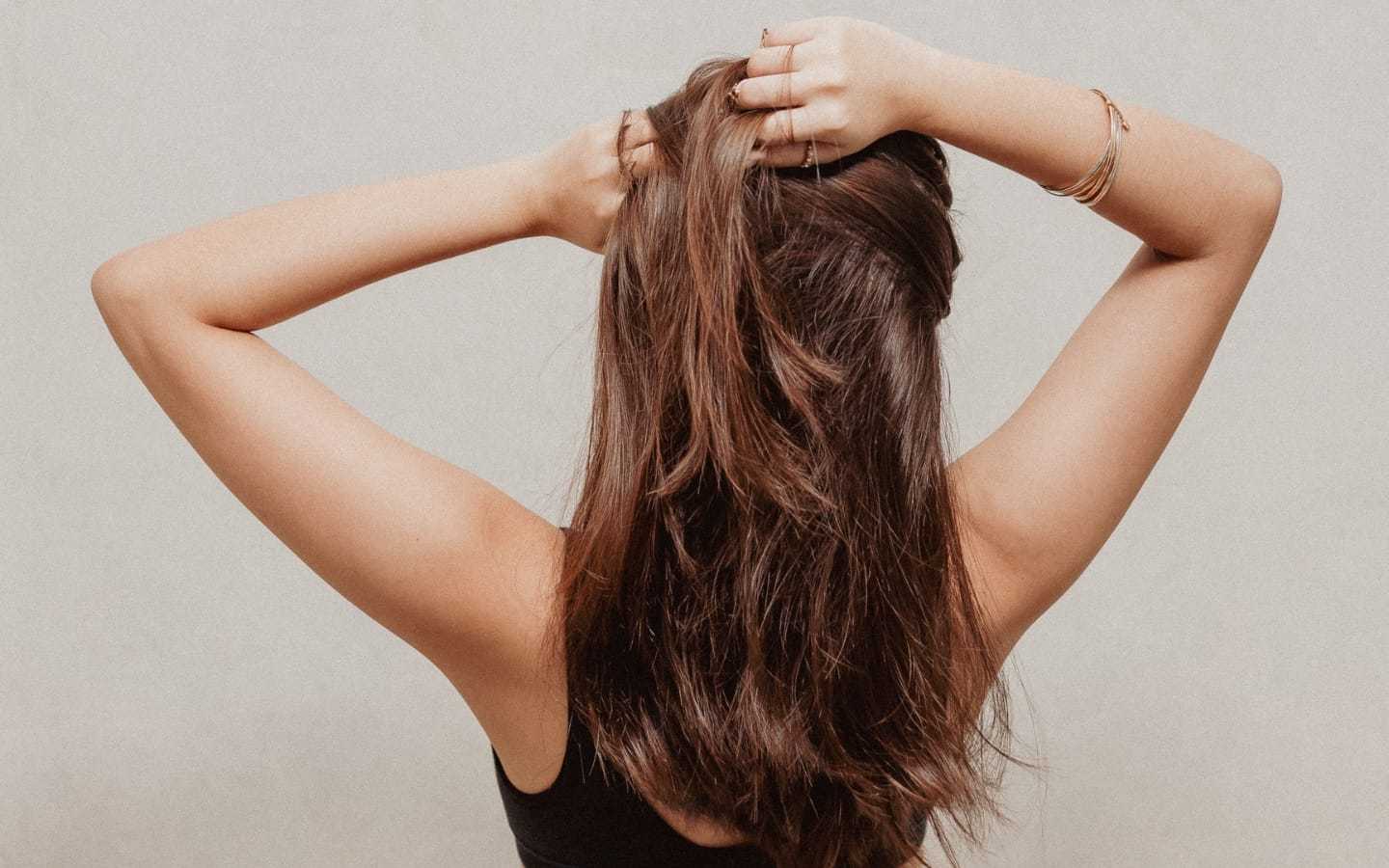 Person with long brown hair, back view, hands lifting hair, wearing bracelets.