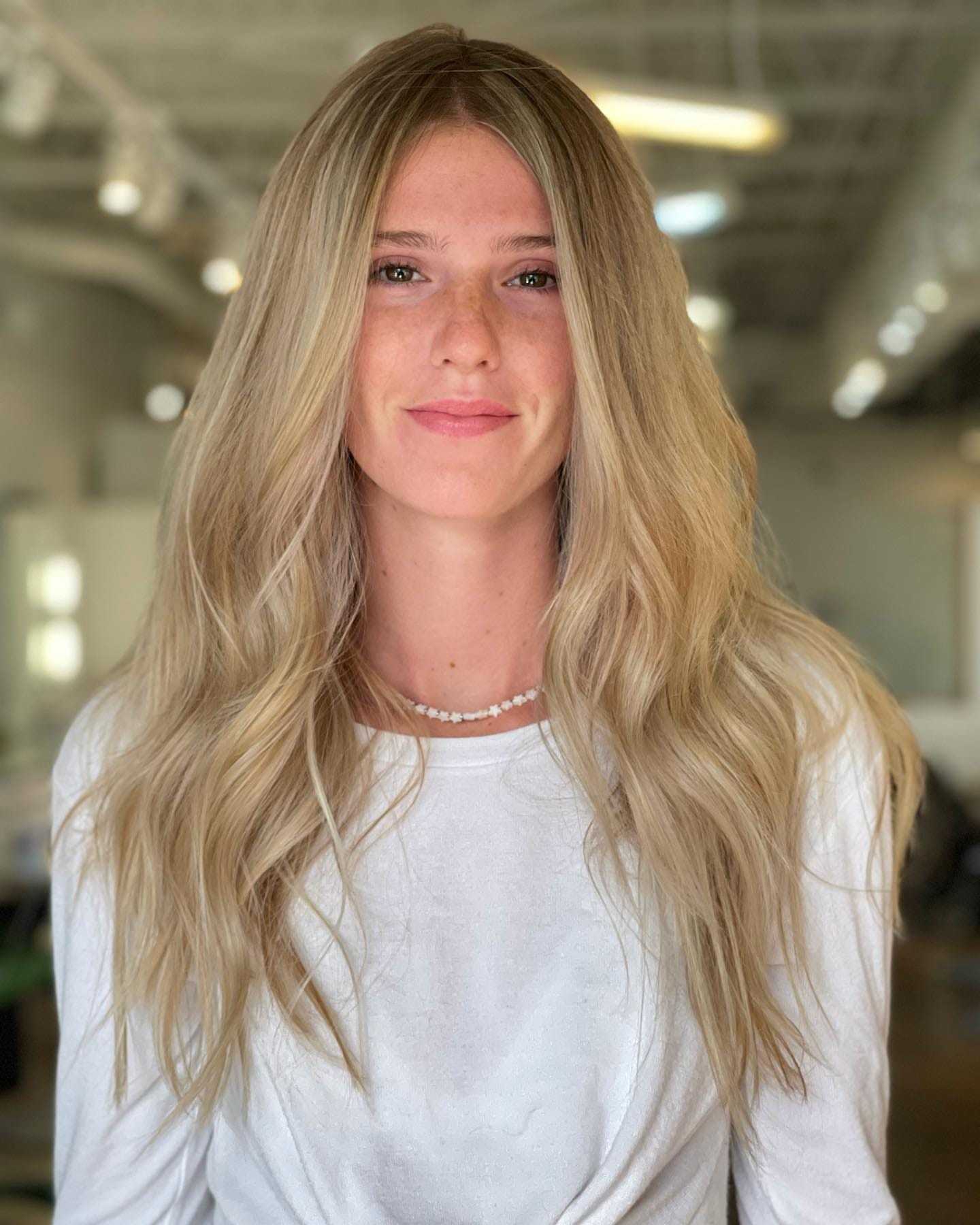 Young woman with long blonde hair smiling in an indoor setting.