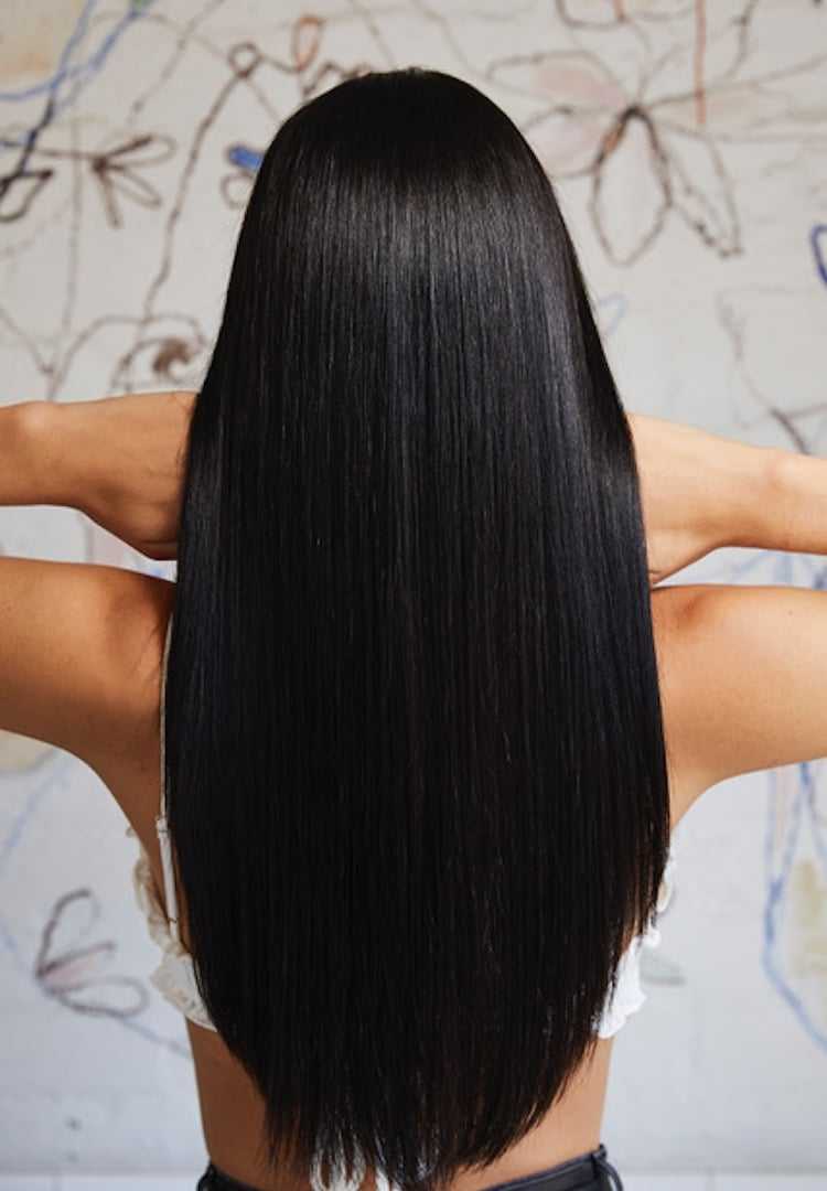 Woman with long, straight black hair facing a wall with abstract art background.