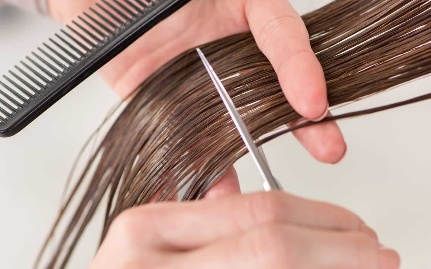Hands cutting wet brown hair with scissors and comb.